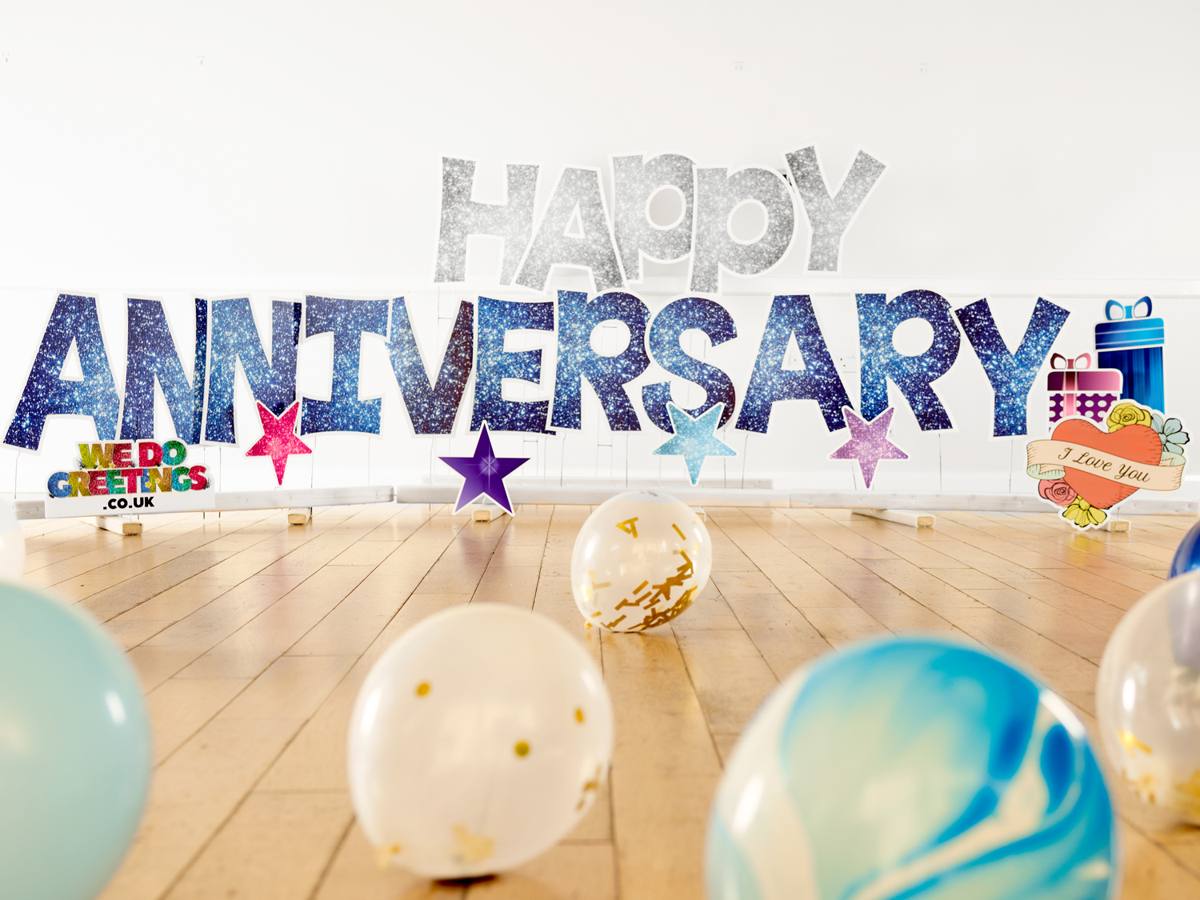 Happy Anniversary in silver glitter letters with balloons on a wooden floor